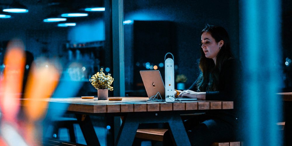 a young woman working in a modern office powering her laptop with a battery pack