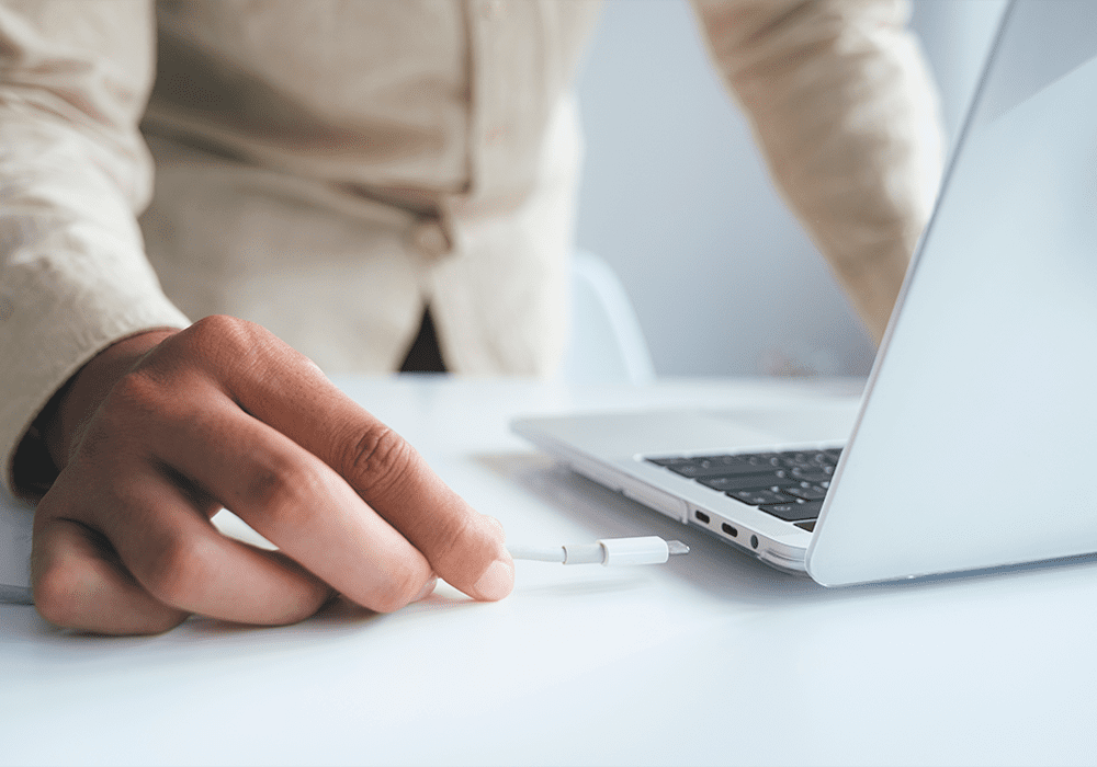 A person working on a laptop connecting to a power cord.